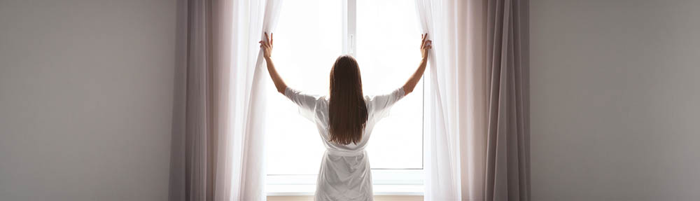 Person opening curtains to morning light, a calm image representing a new day for major depressive disorder